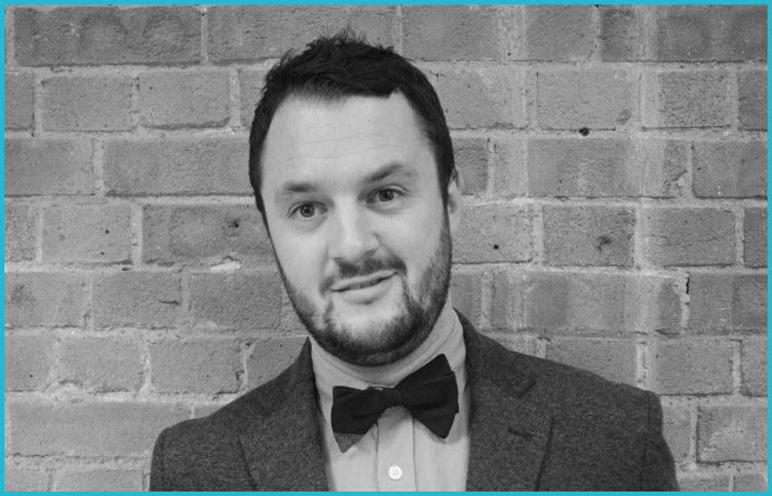 Tom Downes, Senior Contracts Manager at Bay Media smiles gently at the camera, wearing a smart jacket and bow tie.